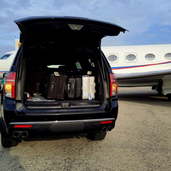 Escalade SUV loaded with luggage beside a private jet on tarmac.