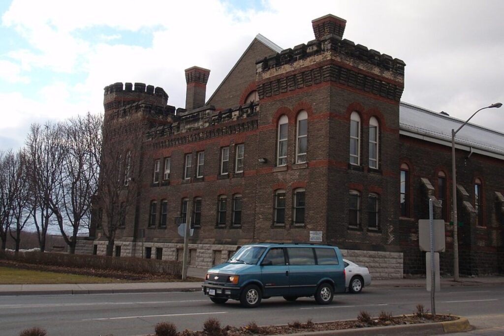 Old stone jailhouse in Guelph with passing cars and overcast skies.