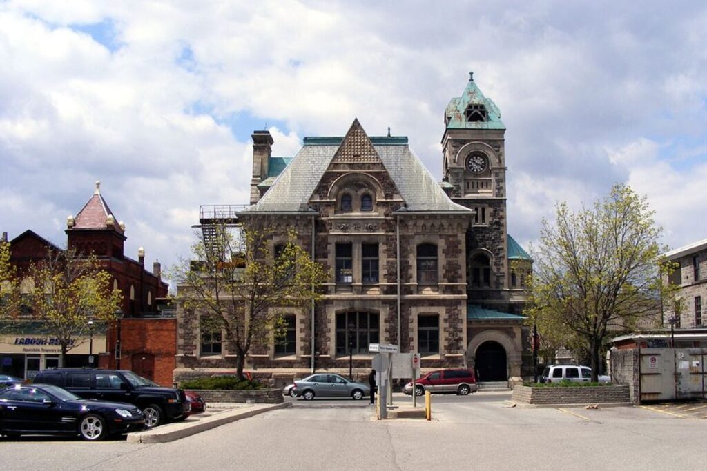 Majestic historic city hall in Guelph framed by trees and parked cars.