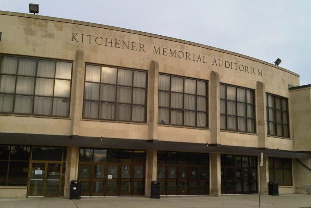 Front entrance of Kitchener Memorial Auditorium under cloudy sky.