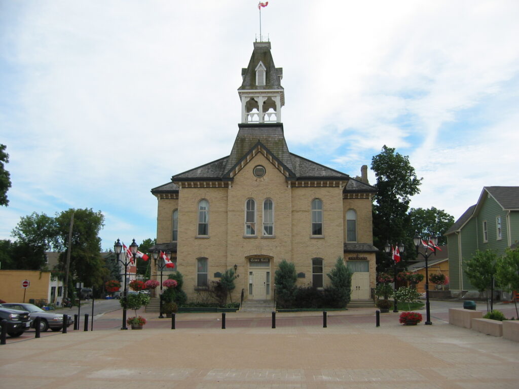 Historic town hall with central tower, Canadian flags, and gardens in Caledon.