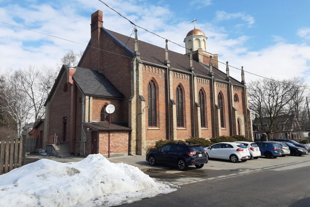 Traditional red-brick church in Milton with parked cars and snow piles nearby.