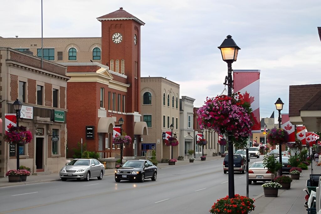 Bowmanville main street with cars, floral planters, and Canadian flags.